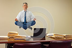 Work related stress relief with yoga as man hovering over stacks of paperwork and computer photo