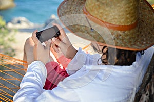 Work & rest: man in hat in a hammock typing on touch phone screen on a summer day
