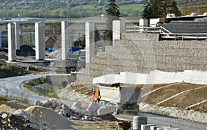 Work site with pillars, sustained wall and trucks driving on the road.