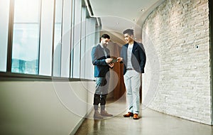 Work smarter, work better. two young businessmen using a digital tablet together in a modern office.