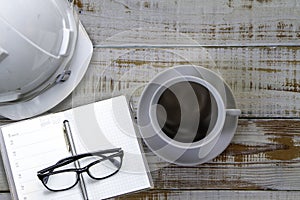 Work space of Engineer safety helmet with notebook, eye glass and cup of coffee  on wooden desk