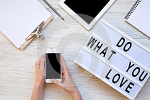 Work space with tablet, female hands, smartphone, clipboard and `Do what you love` word on modern board over white wooden backgr
