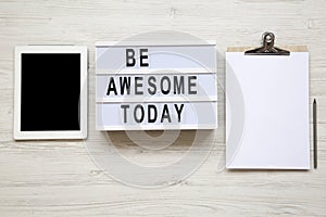 Work space with tablet, notepad and `Be awesome today` word on lightbox over white wooden background, top view.