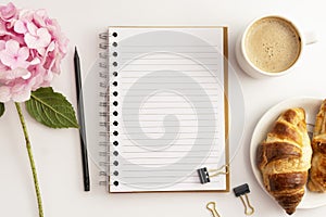 Work space withopen empty notebook, cup of coffee and croissant, pink hydrangea. To do plan