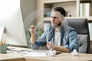 Work Stress. Angry Businessman Sitting At Desk And Crumpling Paper In Office