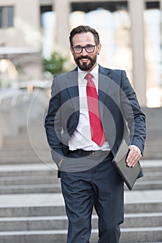 Work on the tablet. Businessman is walking down the street holding mini tablet in hand. Portrait of happy confident businessman