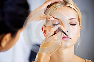 This work takes a steady hand. Pretty young woman having her makeup applied by a stylist.