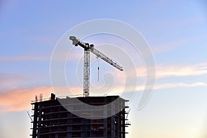 Work of tower crane at construction site against sunset background. Cranes build the high-rise building. New residential