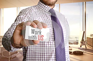 Work with us. Businessman holding a card with a message text written on it