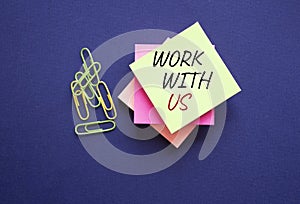 Work with us symbol. Yellow steaky note with paper clips with words Work with us. Beautiful deep blue background. Business and