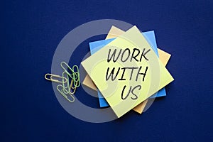 Work with us symbol. Yellow steaky note with words Work with us. Beautiful deep blue background. Business and Work with us concept