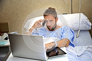 Workaholic business man in hospital room lying in bed sick and injured working with mobile phone computer laptop