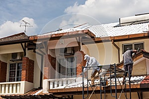 Worker adding undercoat foundation paint onto rooftop with roller at residential building in renovation photo