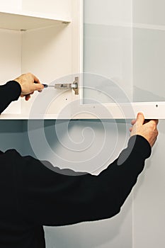 Worker adjusts the loop on the kitchen cabinet with a screwdriver. Installation of kitchen.