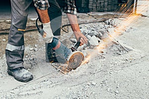 A worker with an angle grinder cuts the concrete pavement of the road, and sparks fly.