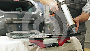 Worker applying an adhesive sealant to car windscreen preparing for replacement