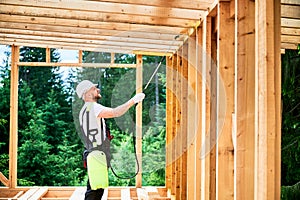 Worker applying fire retardant using sprayer, while constructing wooden frame house near forest