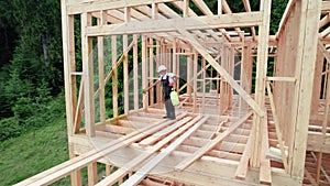 Worker applying fire retardant using sprayer, while constructing wooden frame house near forest