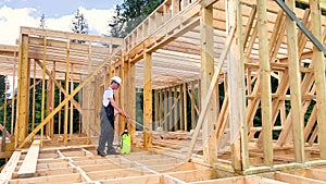 Worker applying fire retardant using sprayer, while constructing wooden frame house near forest