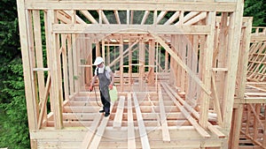 Worker applying fire retardant using sprayer, while constructing wooden frame house near forest