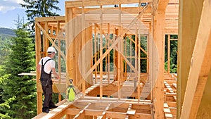 Worker applying fire retardant using sprayer, while constructing wooden frame house near forest