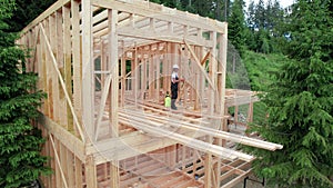 Worker applying fire retardant using sprayer, while constructing wooden frame house near forest