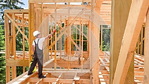 Worker applying fire retardant using sprayer, while constructing wooden frame house near forest