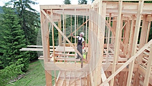 Worker applying fire retardant using sprayer, while constructing wooden frame house near forest