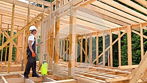 Worker applying fire retardant using sprayer, while constructing wooden frame house near forest