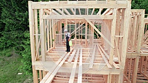 Worker applying fire retardant using sprayer, while constructing wooden frame house near forest