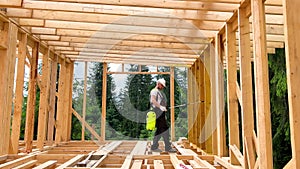 Worker applying fire retardant using sprayer, while constructing wooden frame house near forest