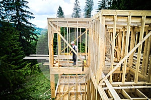 Worker applying fire retardant using sprayer, while constructing wooden frame house near forest