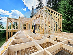 Worker applying fire retardant using sprayer, while constructing wooden frame house near forest