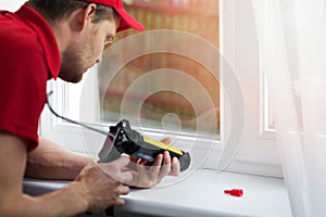 Worker applying silicone sealant under window frame