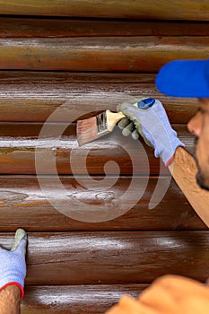 Worker applying stain with a brush on wooden house exterior wall