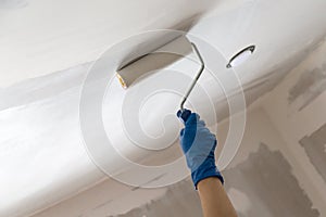 A worker applying whitewash on the ceiling using a roller at home