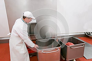 A worker arranged raw meat minced in an industrial process in a stainless steel crate at a meat processing factory