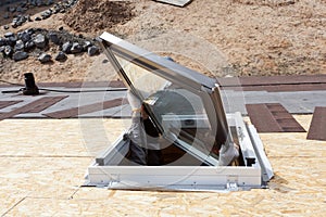 Worker on a asphalt shingle roof installing new plastic mansard or skylight window.