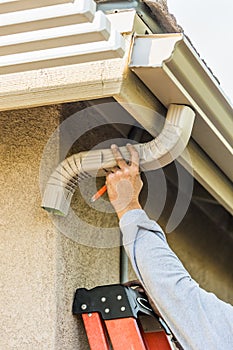 Worker Attaching Aluminum Rain Gutter and Down Spout to Fascia of House