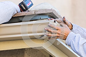 Worker Attaching Aluminum Rain Gutter to Fascia of House.