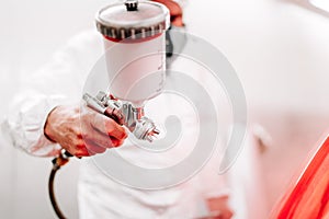 worker and auto mechanic working and painting a red car using spray gun and compressor