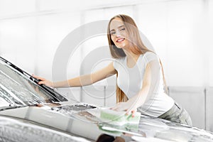 Worker beautiful woman cleaning auto black foam with yellow sponge. Car washing service