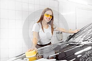 Worker beautiful woman cleaning auto black foam with yellow sponge. Car washing service