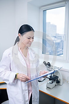 Worker of biochemical laboratory reading her notes