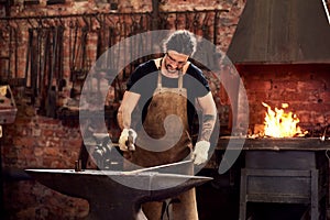 Worker, blacksmith and metal forge in workshop and manual working on hot steel with hammer, fire and sparks. Man