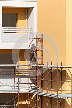 Worker with Blue Hardhat at Work on a Scaffold in a Building Site for the Construction of a Building