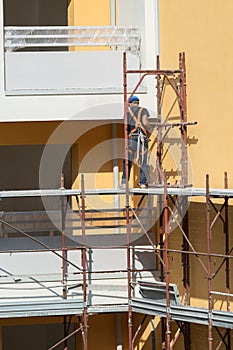 Worker with Blue Hardhat at Work on a Scaffold in a Building Site for the Construction of a Building