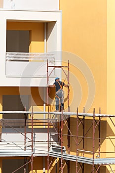 Worker with Blue Hardhat at Work on a Scaffold in a Building Site for the Construction of a Building