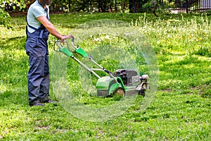 A worker in blue overalls cuts green grass with an industrial petrol mower
