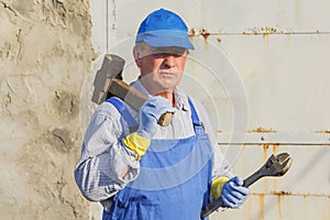 Worker in blue overalls with a sledgehammer and a wrench. Serious look.